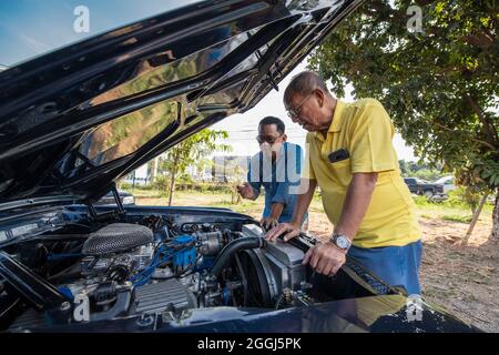 two men looking under the hood of American muscle car in Thailand Stock Photo