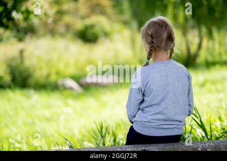 the girl sits with her back and looks into the distance in nature. Stock Photo