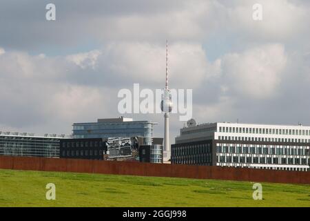 The iconic TV tower of Berlin seen amongst modern buildings and a section iron wall Stock Photo