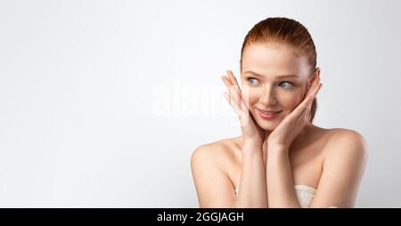 Young Woman Touching Face Posing Wrapped In Towel, Gray Background Stock Photo