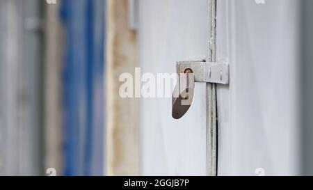 Padlock on a white metal door, close-up with shallow depth of field and soft blurred industrial background. Stock Photo