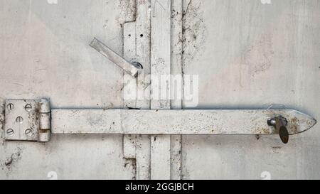Old white metal door with heavy latch and padlock, close-up detail of weathered industrial surface and security hardware. Stock Photo
