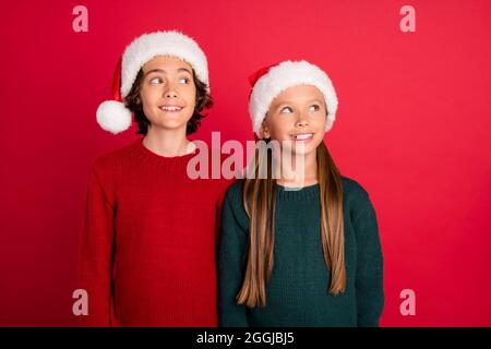 Portrait of two attractive cheerful friends wearing festal cap fantasizing isolated over bright red color background