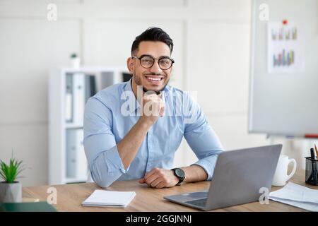 Portrait of happy Arab businessman using laptop computer, making video call, chatting online with colleague at office Stock Photo
