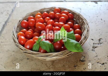 Basket of tomatoes and basil on wooden surface Stock Photo