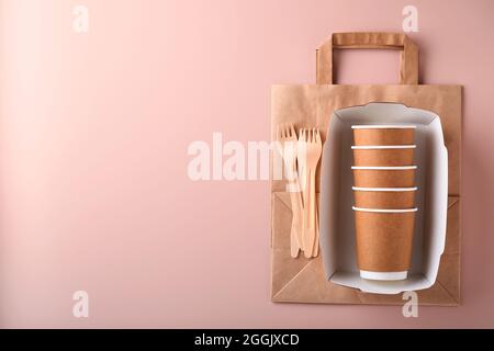 Paper cups, dishes, bag, wooden forks, drinking straws, fast food containers, wooden cutlery on pink background. Eco craft paper tableware. Recycling Stock Photo