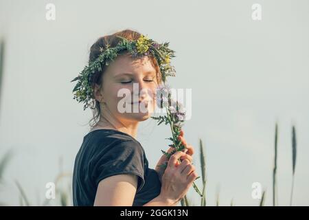Young woman with wreath of natural flowers on her head, dreamy, holds flowers in her hand Stock Photo
