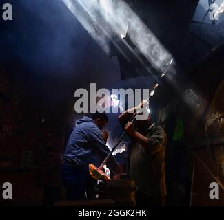 Metal foundry workers in Alexandria pour molten copper into molds in a difficult working environment and high temperatures Alexandria, Egypt. Stock Photo