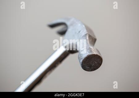 A portrait of the top part of a metal claw hammer isolated on a grey background. The tool is a bit worn by using it for work in construction. Stock Photo