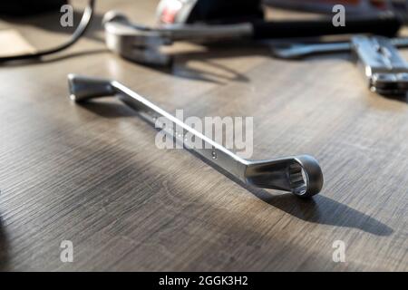 A portrait of a metal chrome box end wrench lying on a wooden table with some other tools lying in the background. The equipment is used for construct Stock Photo