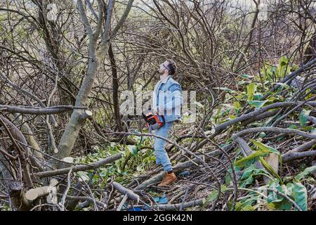 young boy looks at a tree to cut it down with a chainsaw Stock Photo