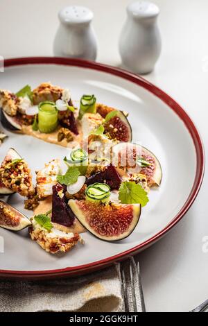 Gourmet salad with ripe figs, goat chevre cheese, fresh cucumber roll, beetroot and mustard leaves with tomato sauce. Summer salad without meat. Delic Stock Photo