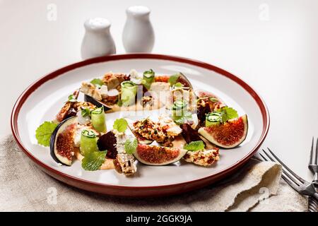 Appetizing gourmet summer salad with ripe figs, goat chevre cheese, fresh cucumber roll, beetroot and mustard leaves with tomato sauce. Summer salad w Stock Photo