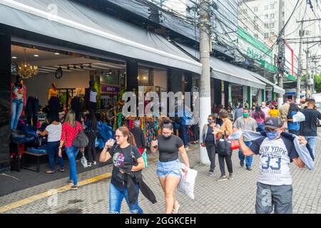 Brazilian people wearing protective face masks as the walk in the market district in Niteroi, Rio de Janeiro, Brazil. A business store is seen in the Stock Photo