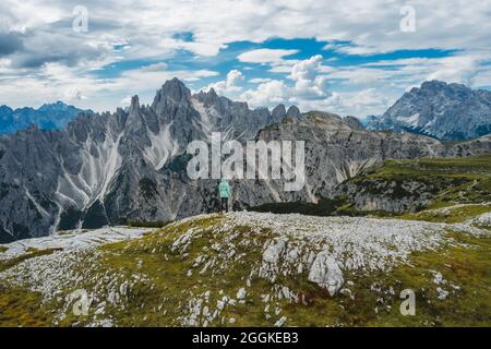 Aerial view of a woman hiker in green jacket against Cadini di Misurina mountain peaks in background. Italian Alps, Dolomites, Italy, Europe Stock Photo