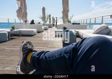 A cross-legged guy enjoying the sunshine in a lounge-bar on the sea Stock Photo