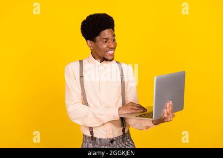 Photo of programmer guy hold laptop look screen wear suspenders shirt isolated yellow color background Stock Photo