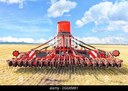 A multifunctional agricultural harrow stands in a harvested wheat field against a blue cloudy sky on a summer day. Stock Photo