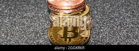 A gold bitcoin coin is lying against a pile of other crypto coins all on a black and white speckled counter top. Stock Photo