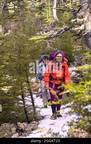 Two young travelers with backpacks are walking along a mountain Stock Photo