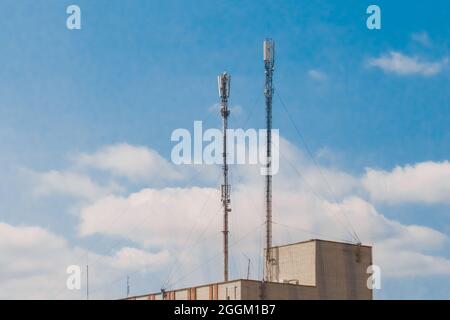 2 mobile cellular telecommunication antennas on the roof of a brick building against a blue sky. Stock Photo