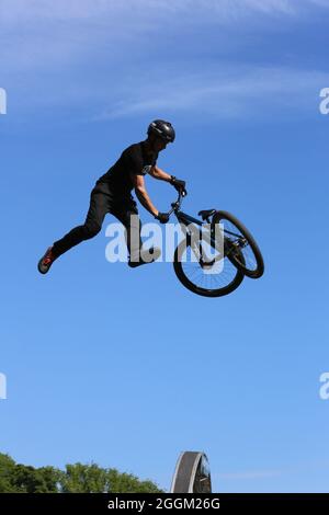 BMX or Mountain Biker high in the air doing a trick during a stunt show set against a mainly bright pale blue sky at the Isle of Man TT Stock Photo
