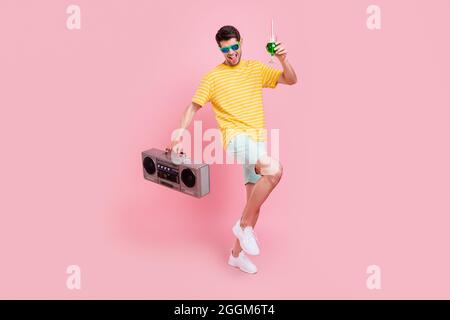 Full size photo of cheerful young happy man hold hands boombox drink dance isolated on pink color background Stock Photo