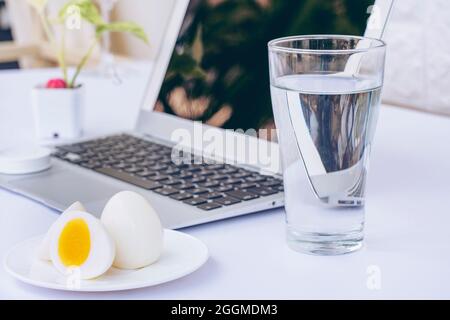 Glass of mineral water with boiled eggs and laptop computer isolated on white background. Dairy diet nutrition healthy eating. Stock Photo
