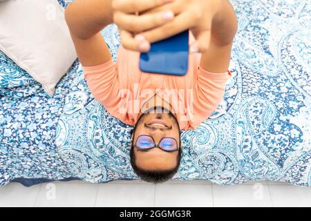 young latino man lying in bed holding smart phone Stock Photo