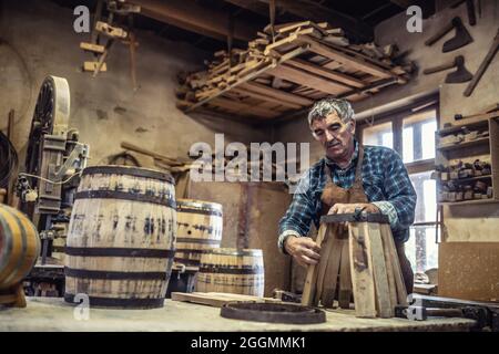 Woodworker prepares timber basis for handmade wooden barrel manufacturing in his rusti workshop. Stock Photo