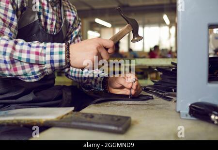 Shoe factory worker sitting at table, making new leather boots and using hand hammer Stock Photo