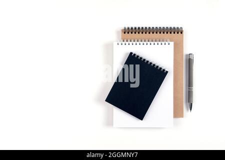 Three blank notepads on a spiral stacked in a stack on a white background. Notebooks with white, black and recycled sheets and pen. Education, office. Stock Photo