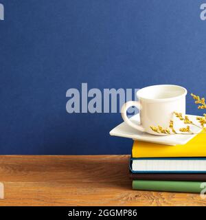 Stack of notebooks and coffee cup on wooden desk. blue wall background Stock Photo