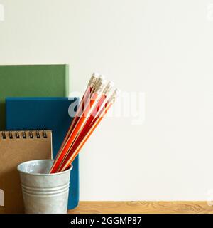 Notebooks, orange pencils on wooden desk. ivory wall background Stock Photo