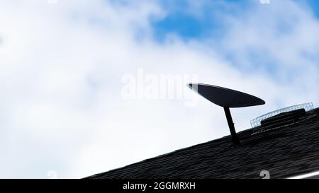 A dark silhouette of a SpaceX Starlink satellite dish, an all-new satellite internet constellation service, is seen mounted on the roof of a home. Stock Photo