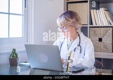Shot of  female doctor working with her laptop in the consultation. Portrait of caucasian woman using computer on desktop in home office - Professiona Stock Photo