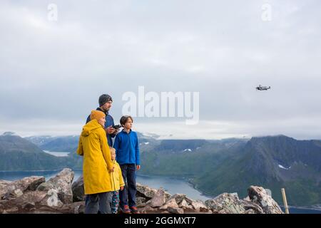 Happy family, standing on a rock and looking over Segla mountain on Senja island, North Norway, taking pics with drone. Amazing beautiful landscape an Stock Photo