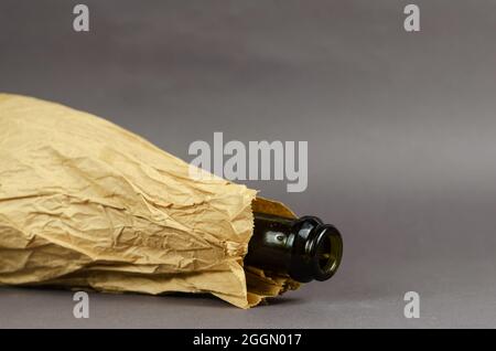 Drunken Bottle in paper bag lies on gray background. Dark empty bottle of alcohol in crumpled brown bag. Social problem of alcoholism concept. Close-u Stock Photo
