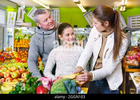 Parents with daughter choosing sweet bananas in fruit market Stock Photo