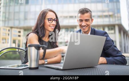 Two office, administration, finance or lawyers discuss work strategy looking into a laptop outdoors, smiling. Stock Photo