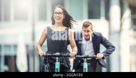 Two work colleagues having fun on electric scooters chasing one another in the city. Stock Photo