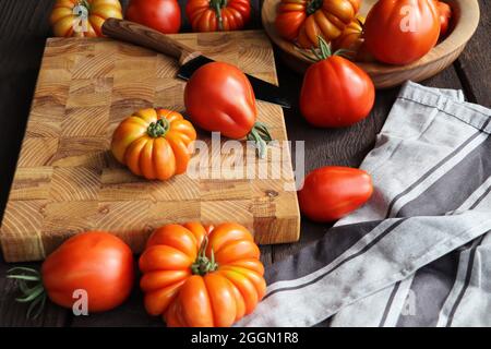 Fresh ripe hairloom tomatoes and knife on rustic wooden board over dark background Stock Photo
