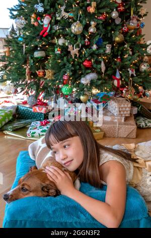 Eight year old girl laying with her dog in front of the Christmas tree Stock Photo