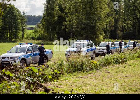 Police officers next to the village of Usnarz Gorny are standing on guard on the field next to a makeshift camp where a group of migrants stay and not being let into the Polish side. The Polish government is introduce a State of Emergency on the border with Belarus in two voivodeships (the highest-level administrative division of Poland) to stop migrants crossing illegally. Under a state of emergency, Polish authorities will have the power to restrict the movement of people, including aid organisations or press in border areas. It's the first such measure since the 1981 declaration of martial Stock Photo