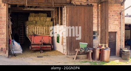 agricultural objects in front of a barn of an old farmhouse with grain crasher, silage wagon and barrels Stock Photo