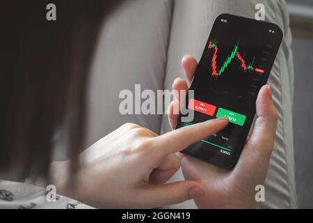 Analysis of the stock market and cryptocurrency charts by using mobile phone app. Woman with smartphone and financial graphs on the screen. Business a Stock Photo