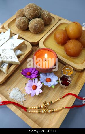 Indian festival Raksha bandhan. Rakhi thali with diya, flowers and tilak with assorted Sweets such as Gulab Jamun, Kaju katli, and Churma Laddo. Stock Photo
