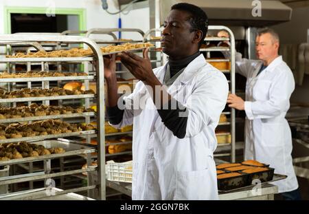 African baker arranging trays with bakery products on trolley Stock Photo