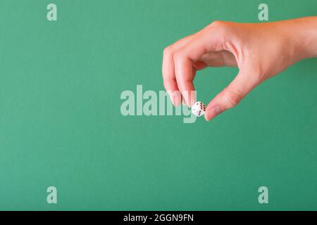 Female hand holds a white dice on a green background. Idea for gambling, casino, dice games. Stock Photo