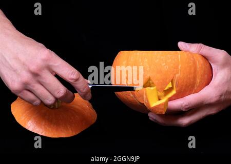 Step 3 Cutting eyes and mouth in a pumpkin with a knife to prepare Jack's lantern, isolated on black background, close-up, copy space. Step-by-step in Stock Photo